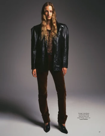 Model Kira Alferink in a black leather blazer and brown trousers standing against a gradient grey backdrop for Grazia Germany.