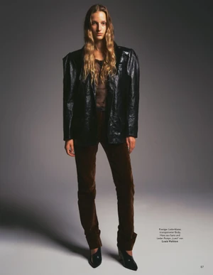 Model Kira Alferink in a black leather blazer and brown trousers standing against a gradient grey backdrop for Grazia Germany.