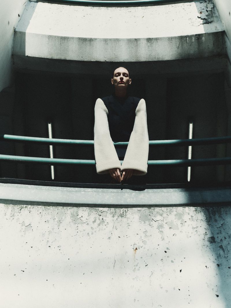 Model leaning on a teal railing against a weathered concrete architectural background with dramatic shadows.