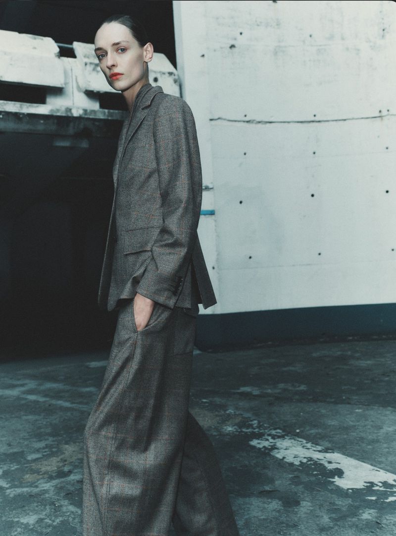 Model wearing a grey trouser suit standing against an industrial concrete wall in a fashion cover editorial by Gus&Lo for Sèduction Magazine