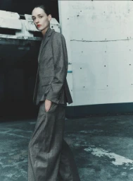 Model wearing a grey trouser suit standing against an industrial concrete wall in a fashion cover editorial by Gus&Lo for Sèduction Magazine