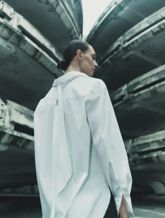 Model Daga Ziober wearing an oversized white button-up shirt standing in front of concrete architectural structures.