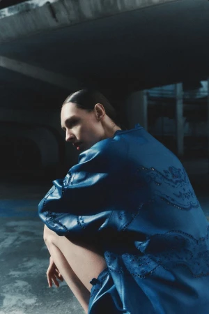 Model Daga Ziober wearing a blue leather jacket crouching beneath concrete architecture
