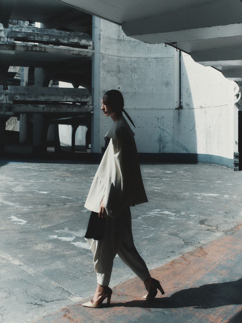 Model wearing white layered outfit walking in a concrete multi-story car park