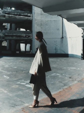 Model wearing white layered outfit walking in a concrete multi-story car park