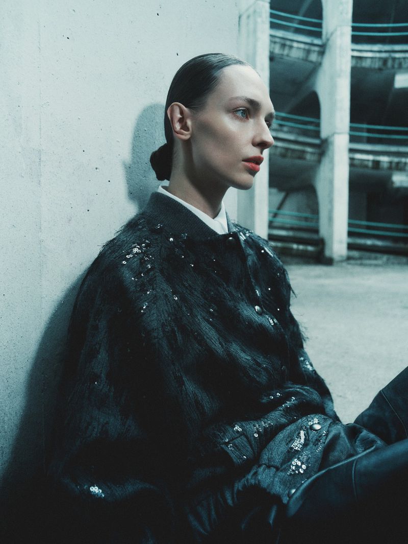 Model Daga Ziober wearing a dark embellished jacket seated against a concrete wall for Seduction Magazine.