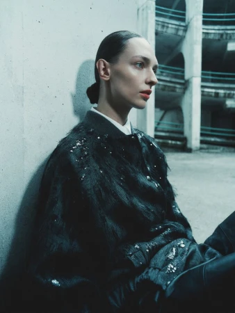 Model Daga Ziober wearing a dark embellished jacket seated against a concrete wall for Seduction Magazine.