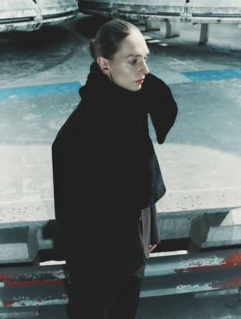Model Daga Ziober wearing a heavy black coat standing outdoors against an industrial concrete background for Sèduction Magazine.