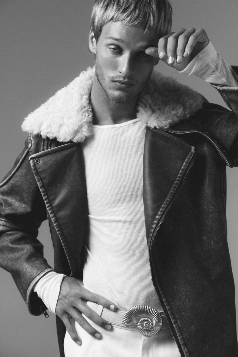 Model Yeray Allgayer in a dark shearling jacket and white shirt posing against a grey studio backdrop.