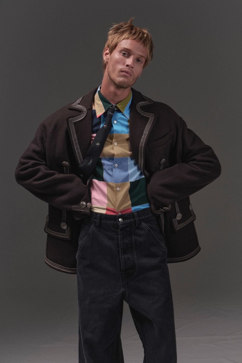 Model Yeray Allgayer in a dark jacket, patterned shirt, and dark trousers against a grey backdrop for Numero Netherlands.