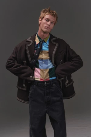 Model Yeray Allgayer in a dark jacket, patterned shirt, and dark trousers against a grey backdrop for Numero Netherlands.
