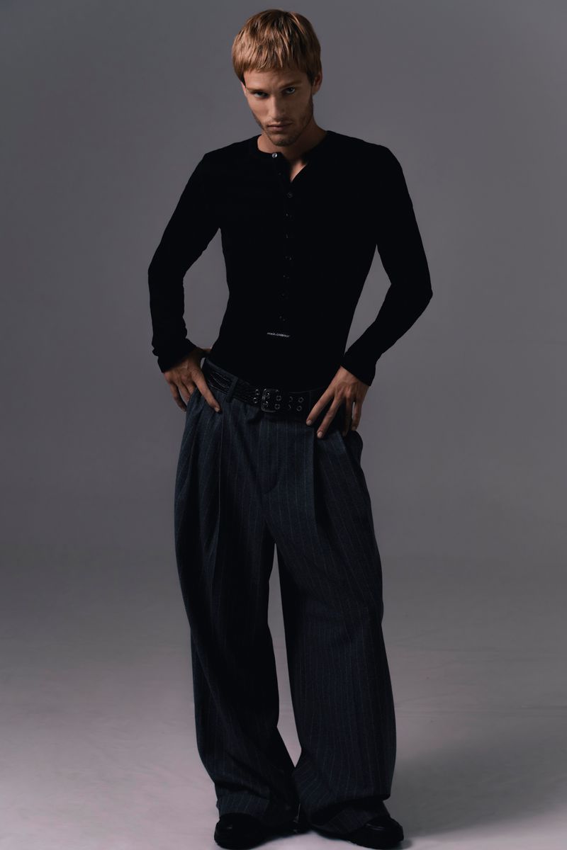 Model Yeray Allgayer wearing a black henley top and wide trousers against a grey studio backdrop for Numero Netherlands.