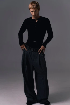 Model Yeray Allgayer wearing a black henley top and wide trousers against a grey studio backdrop for Numero Netherlands.