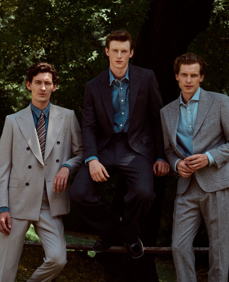 Three male models in tailored suits and dress shirts posing outdoors in front of leafy trees for Gentleman Magazine.