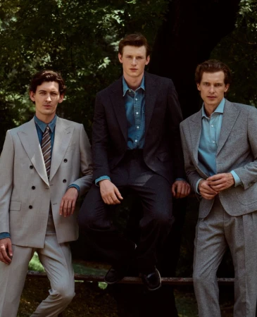 Three male models in tailored suits and dress shirts posing outdoors in front of leafy trees for Gentleman Magazine.