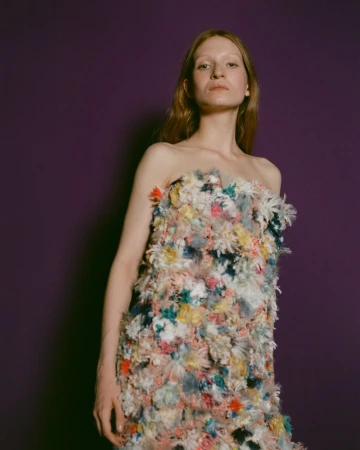 Model wearing a strapless textured multicolored dress against a solid dark purple studio background