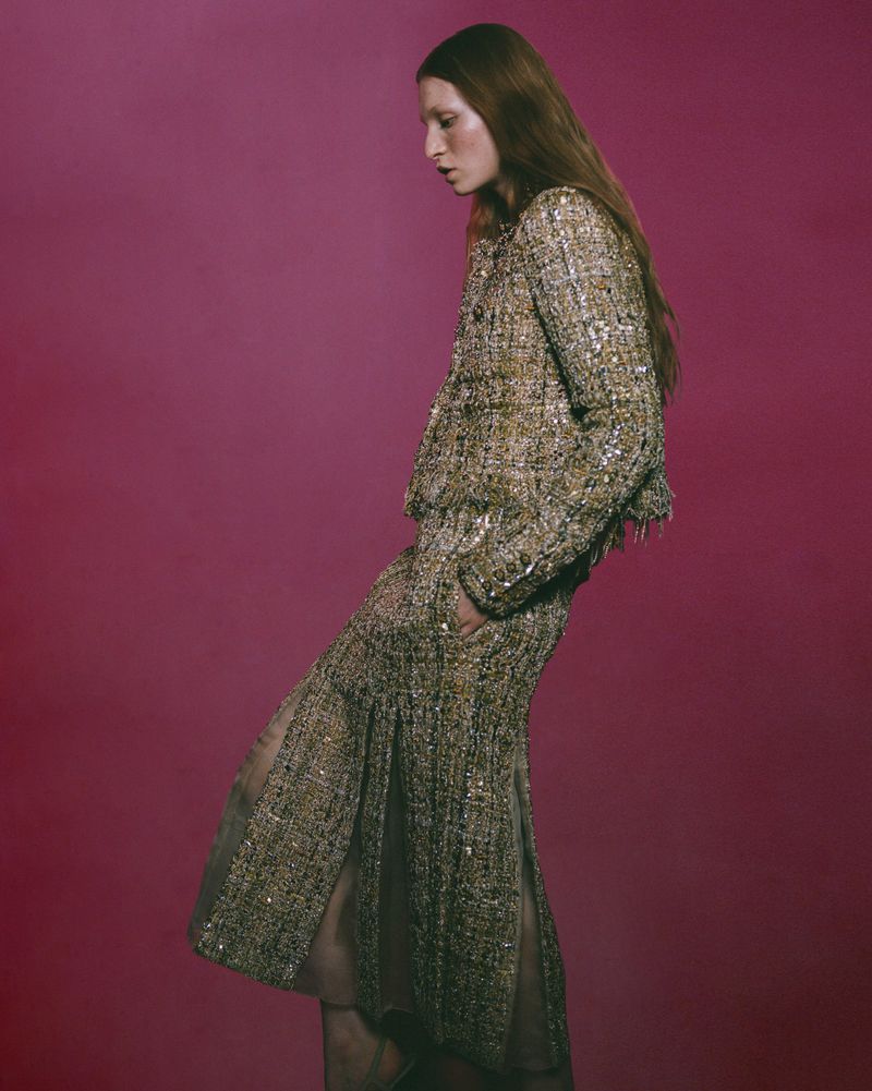 Model wearing a textured metallic tweed jacket and matching skirt against a dark pink background for Russh.