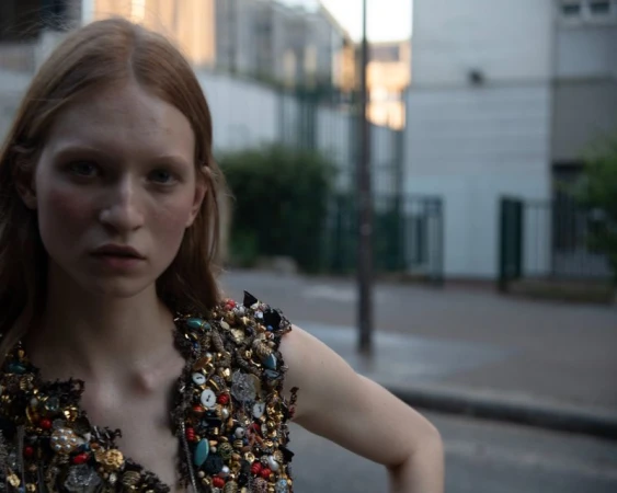 Model with red hair wearing an embellished couture garment featuring beads and stones outdoors on a city street