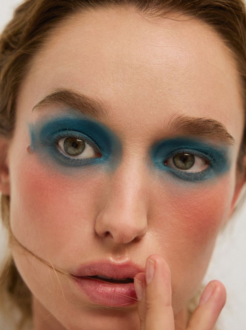 Close-up portrait of a woman wearing bold blue eyeshadow and blush for a beauty editorial by Russh.
