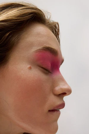 Close-up profile of a woman with vibrant pink eyeshadow across her eyes and nose bridge against a plain white background