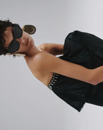 Model in dark sunglasses and black top against a grey seamless background