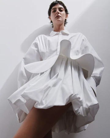 Model in a voluminous white sculptural dress against a white studio background shot from a low angle.