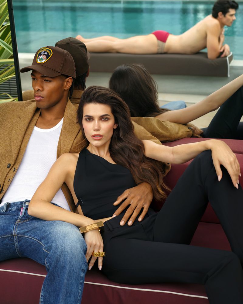 Woman in black top seated beside a man in a brown cap and jacket near a poolside lounge