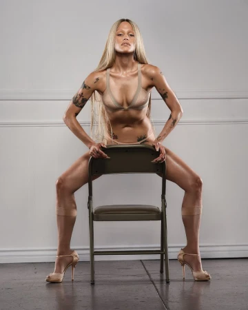 Model Gabbriette posing straddling a folding chair wearing beige undergarments and heels