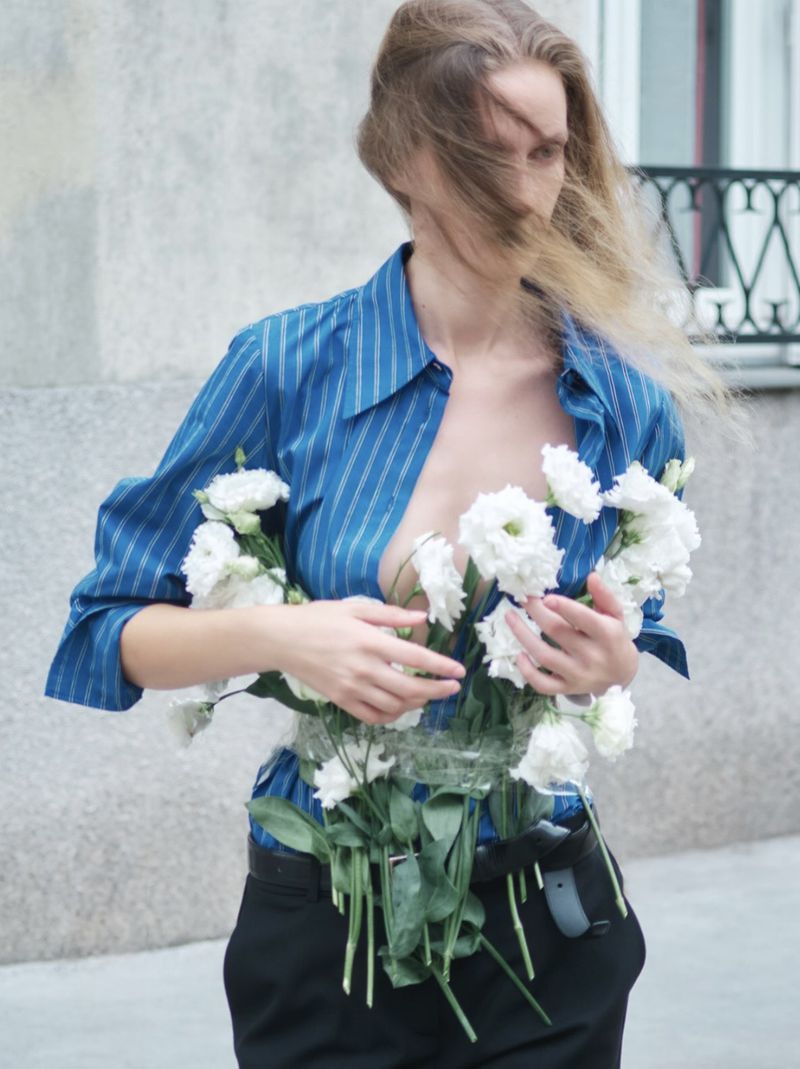 Model wearing blue striped shirt and black trousers holding white flowers for D Repubblica editorial