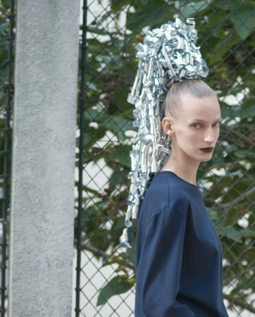 Model with silver ribbon hair accessory wearing a navy blue top against a wire fence