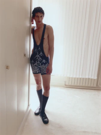 Model standing indoors wearing a printed dark romper with high socks and loafers against a pale interior background.