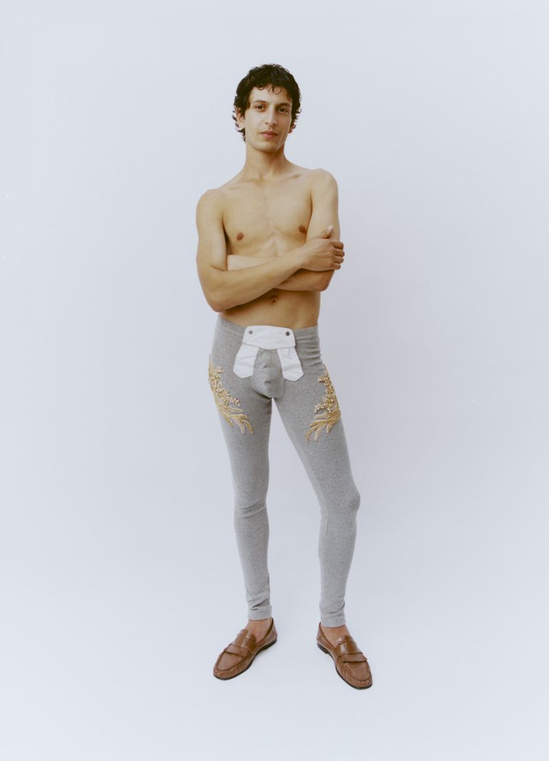 Shirtless male model wearing grey patterned long johns and brown loafers against a plain white seamless backdrop.