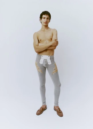 Shirtless male model wearing grey patterned long johns and brown loafers against a plain white seamless backdrop.