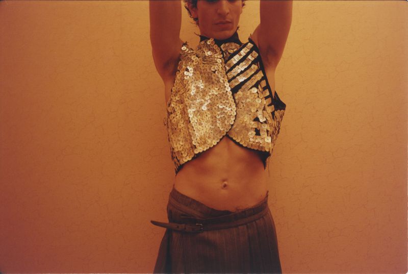 Close-up of a model wearing a sequined vest and trousers against a warm solid background