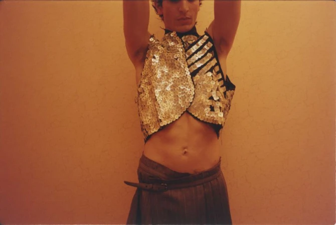 Close-up of a model wearing a sequined vest and trousers against a warm solid background