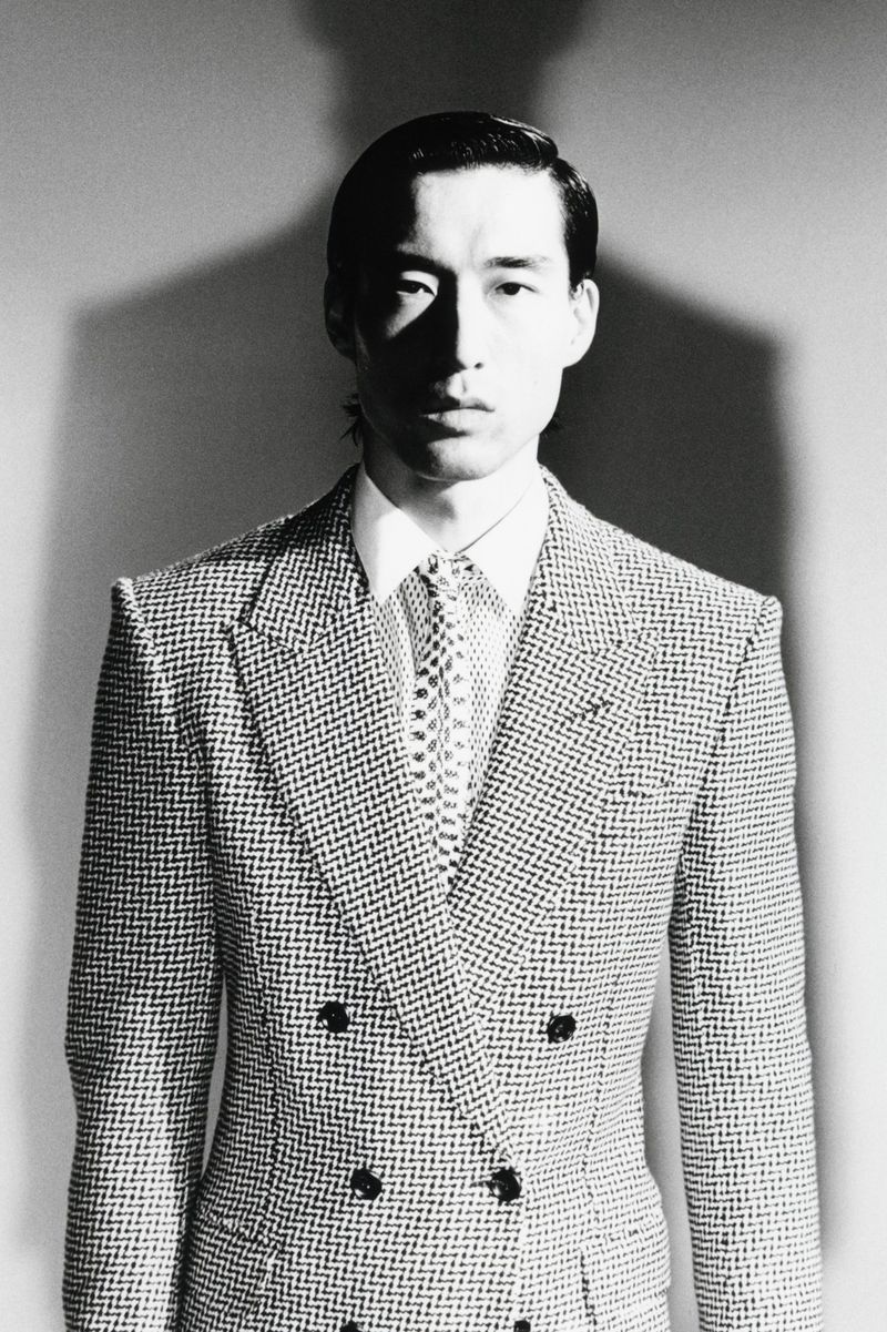 Monochrome portrait of a man wearing a double-breasted patterned suit jacket, white shirt, and patterned tie against a plain backdrop.