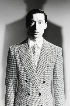 Monochrome portrait of a man wearing a double-breasted patterned suit jacket, white shirt, and patterned tie against a plain backdrop.