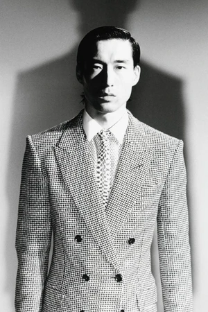 Monochrome portrait of a man wearing a double-breasted patterned suit jacket, white shirt, and patterned tie against a plain backdrop.