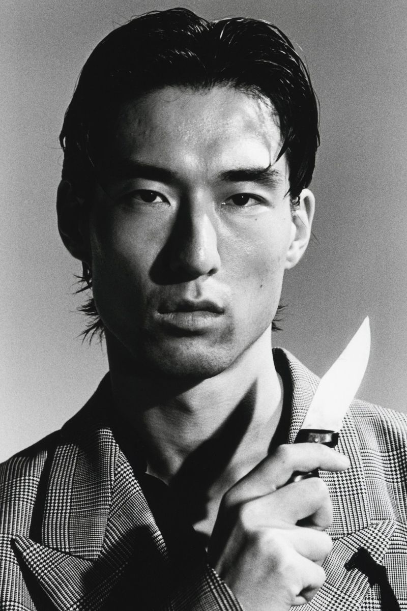 Close-up portrait of a man holding a knife, wearing a plaid blazer, shot in monochrome for HERO Magazine.