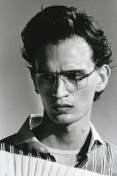 Close-up black and white portrait of a man wearing striped shirt and wire-rimmed glasses against a light background