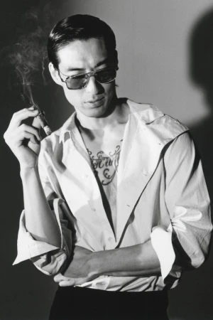 Monochrome portrait of a man wearing sunglasses holding a lit cigar in front of a plain background.