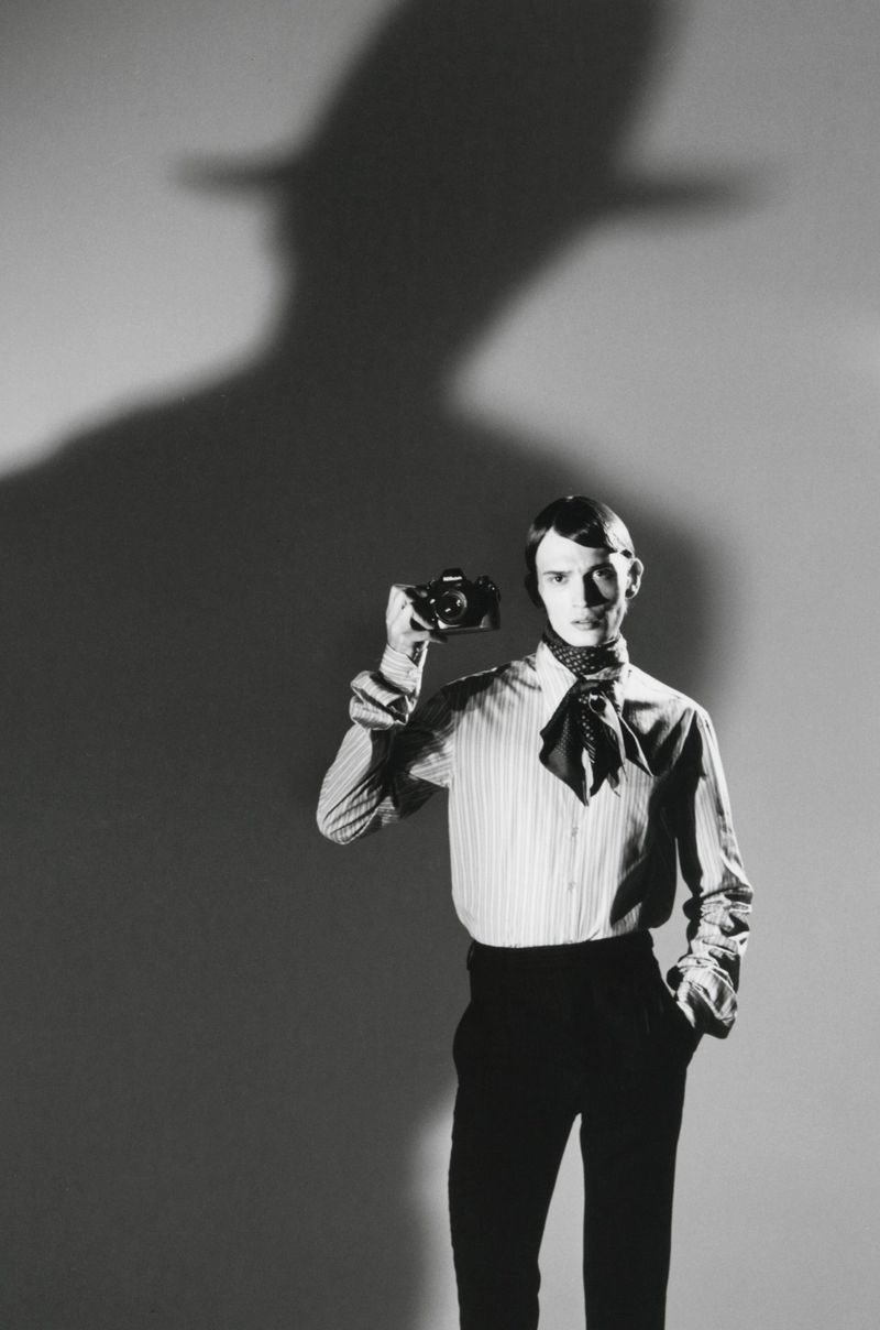 Monochrome portrait of a male model holding a camera in front of a wall with a dramatic silhouette shadow