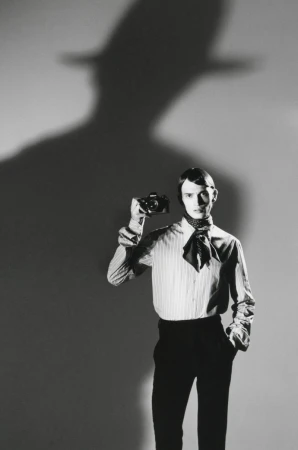 Monochrome portrait of a male model holding a camera in front of a wall with a dramatic silhouette shadow