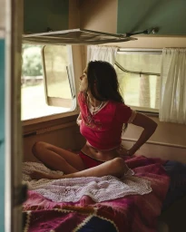 Woman sitting cross-legged on a bed inside a retro camper van looking out the open window