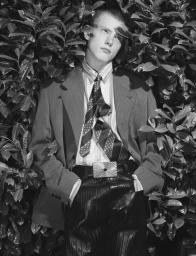 Monochrome portrait of a young man wearing a patterned tie and suit jacket amidst dense foliage for Replica Man Magazine.