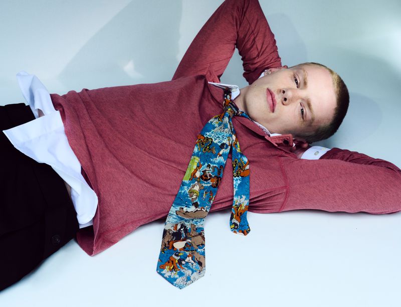 Model Joel Kemp lying down wearing a red shirt and patterned blue tie for Replica Man Magazine
