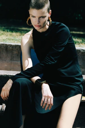 Model with short hair wearing a black top and trousers outdoors in a park setting for Armarium Spring Summer 2027.