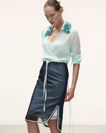 Model in mint green blouse with ruffled collar and dark pinstriped midi skirt against a plain white studio background.