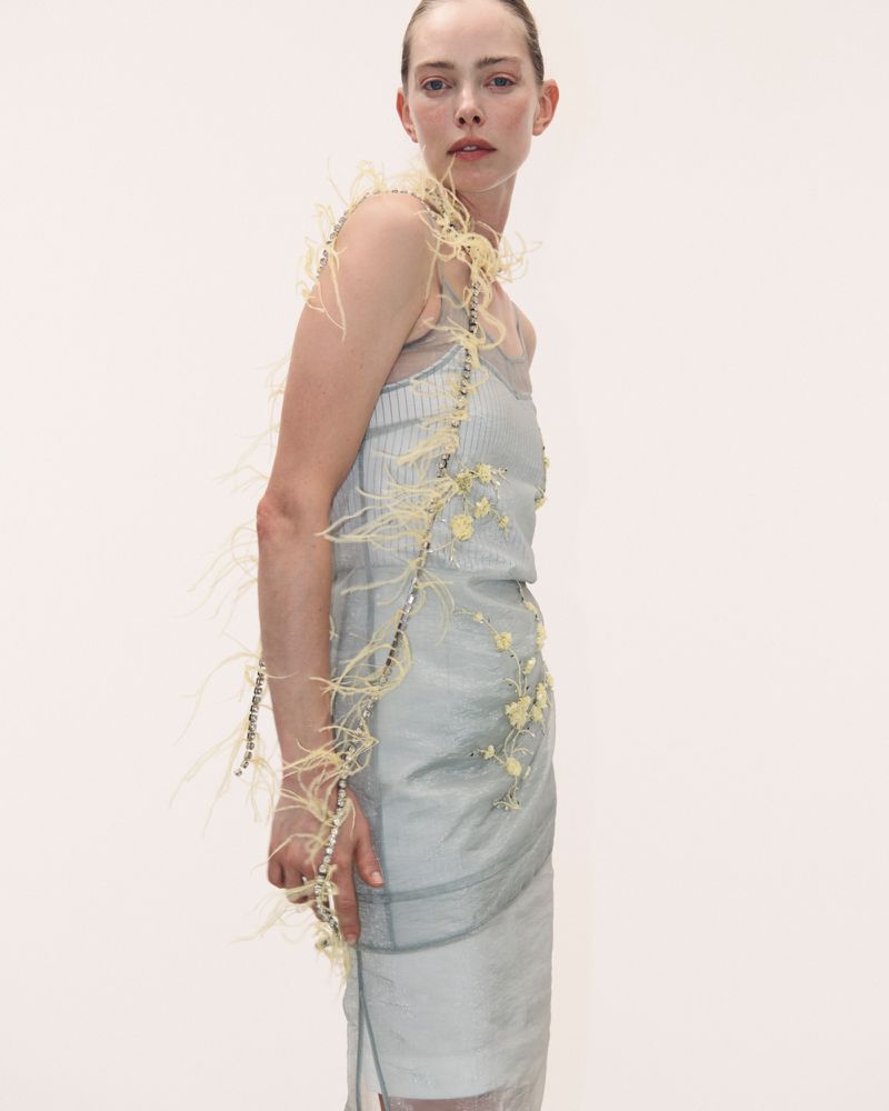 Model in feather-trimmed pale blue dress against a plain neutral background for Des Phemmes Spring/Summer 2027.