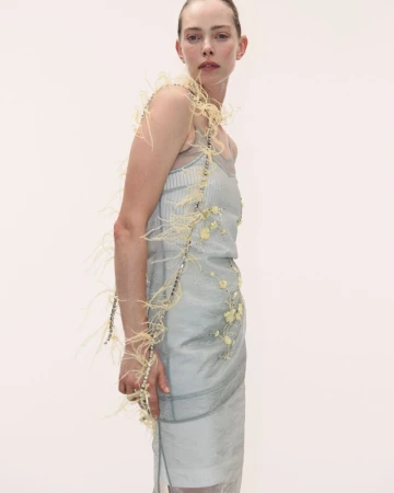 Model in feather-trimmed pale blue dress against a plain neutral background for Des Phemmes Spring/Summer 2027.